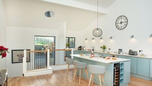 Une cuisine moderne dotée d’un îlot central, de tabourets de bar, de luminaires suspendus et d’une grande fenêtre.