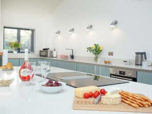 A modern kitchen with a white countertop, a wine bottle, glasses, a bowl of grapes, cheese, and a cutting board with a knife.