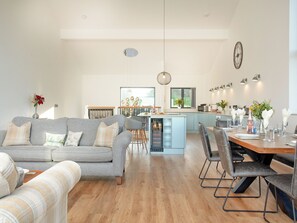 A modern living room with a grey sofa, a dining area with a wooden table, and a kitchen in the background.