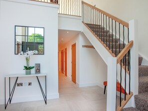 A modern interior with a staircase, a mirror, a console table with a vase of flowers, and a hallway leading to another room.