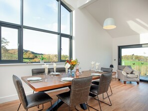 Ein Essbereich mit einem Holztisch, gedeckt für sechs Personen, großen Fenstern und Blick auf die Landschaft.