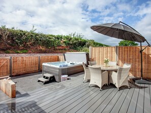 A deck with a hot tub, outdoor furniture, and a table with an umbrella.