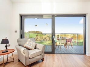 A living room with a sofa, a table, and a balcony with a view of a green landscape.