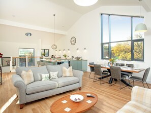 A spacious living area with a grey sofa, wooden coffee table, and a dining area with chairs and a table.