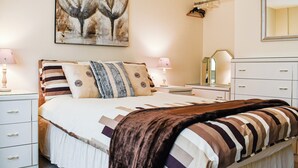 A neatly arranged bedroom with a large bed, bedside tables, a dresser, and a painting on the wall. - Between the forest and the sea (New Milton, near Lymington)