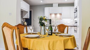 A dining table set for six with a yellow tablecloth, six chairs, and a bottle of wine. - Between the forest and the sea (New Milton, near Lymington)
