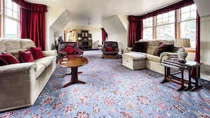 A spacious living room with a high ceiling, large windows with red curtains, and a floral carpet. - Fourpenny Cottage - UK34744 (Skelbo, near Dornoch)