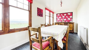 A dining area with a table set for four, wooden chairs, a red curtain, and a view of the countryside. - Fourpenny Cottage - UK34744 (Skelbo, near Dornoch)