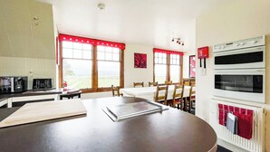 A kitchen with a large window, a dining table, and a built-in oven. - Fourpenny Cottage - UK34744 (Skelbo, near Dornoch)