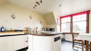 A kitchen with a curved island, a dining table with chairs, and a window with a view of the outdoors. - Fourpenny Cottage - UK34744 (Skelbo, near Dornoch)