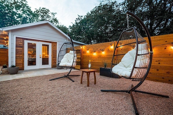 Un rincón al aire libre acogedor con dos sillones de mimbre, una mesa de madera pequeña y una botella de vino.