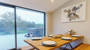 A dining area with a wooden table set for six, a hot tub outside, and a large window.