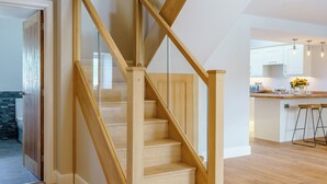 A wooden staircase with glass railings leading to a kitchen area.