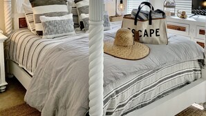 Un dormitorio ordenado con una cama con dosel, un ventilador de techo y un televisor sobre una mesita.