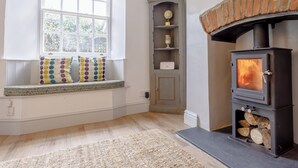 Una habitación acogedora con chimenea, una ventana adornada con un volante floral y un banco con cojines coloridos.