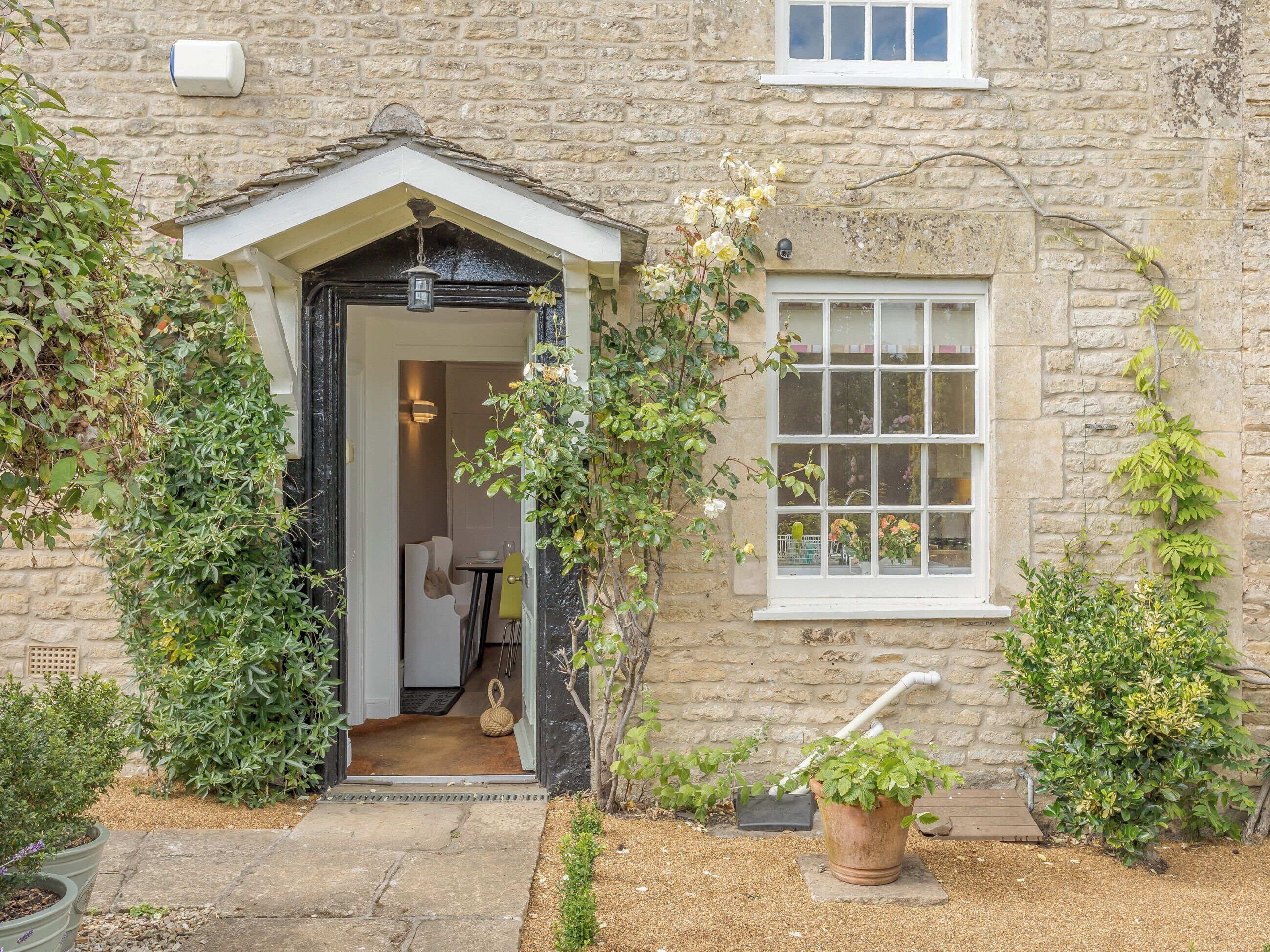 A stone building with a door leading to an interior space, a window, and a small garden area with plants and a wooden deck.