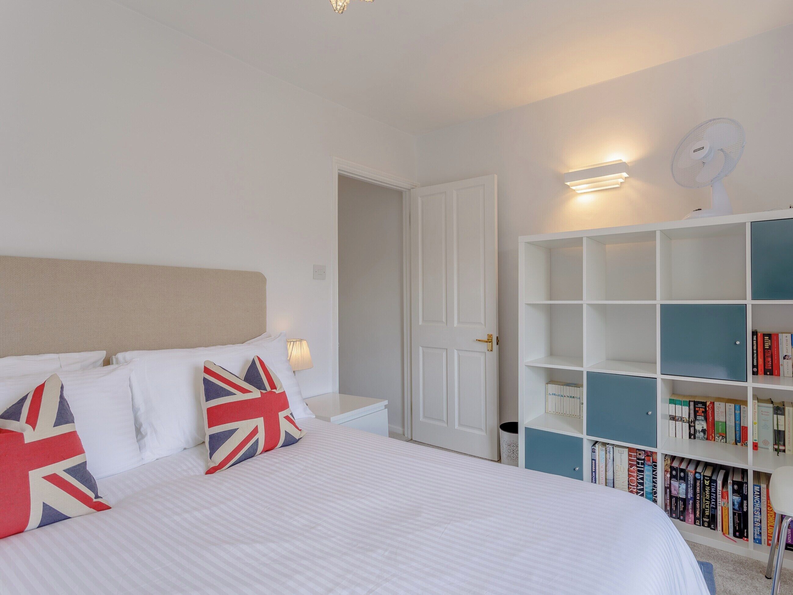 A neatly arranged bedroom with a bed, bedside tables, a bookshelf, and a door.