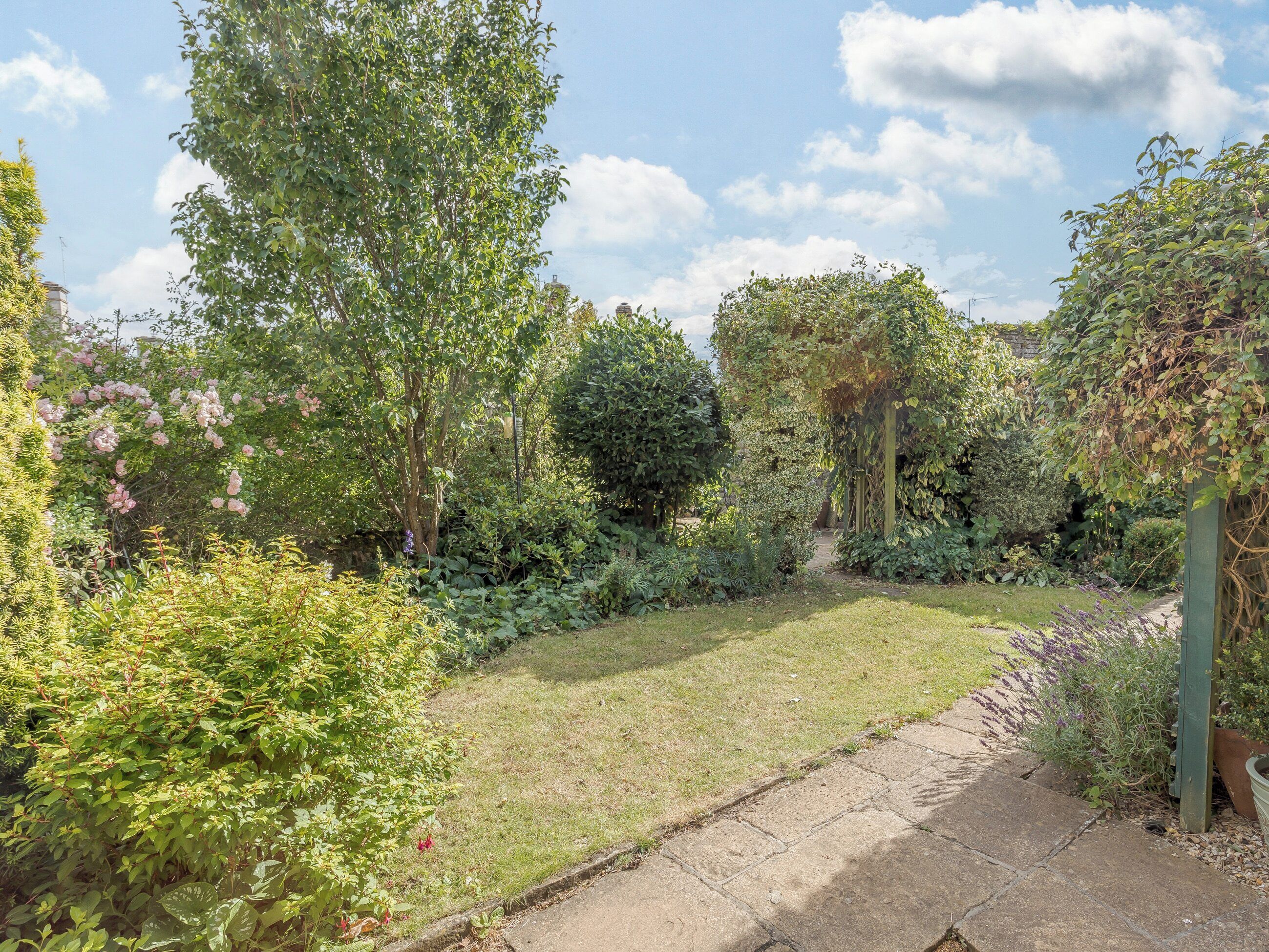 A well-maintained garden with a variety of plants and trees, a clear pathway, and a grassy area.