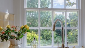 Cocina con un lavamanos blanco, un grifo de acero inoxidable y una ventana con vistas al verdor.