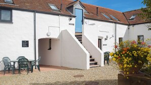 A building with a white exterior, a blue door, and a staircase leading to an upper level. There are outdoor seating areas with chairs and a table. - Seascape Cottage - UK6725 (Lydstep, near Tenby)