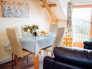 A dining area with a table set for four, a coffee pot, and a vase with flowers. - Seascape Cottage - UK6725 (Lydstep, near Tenby)