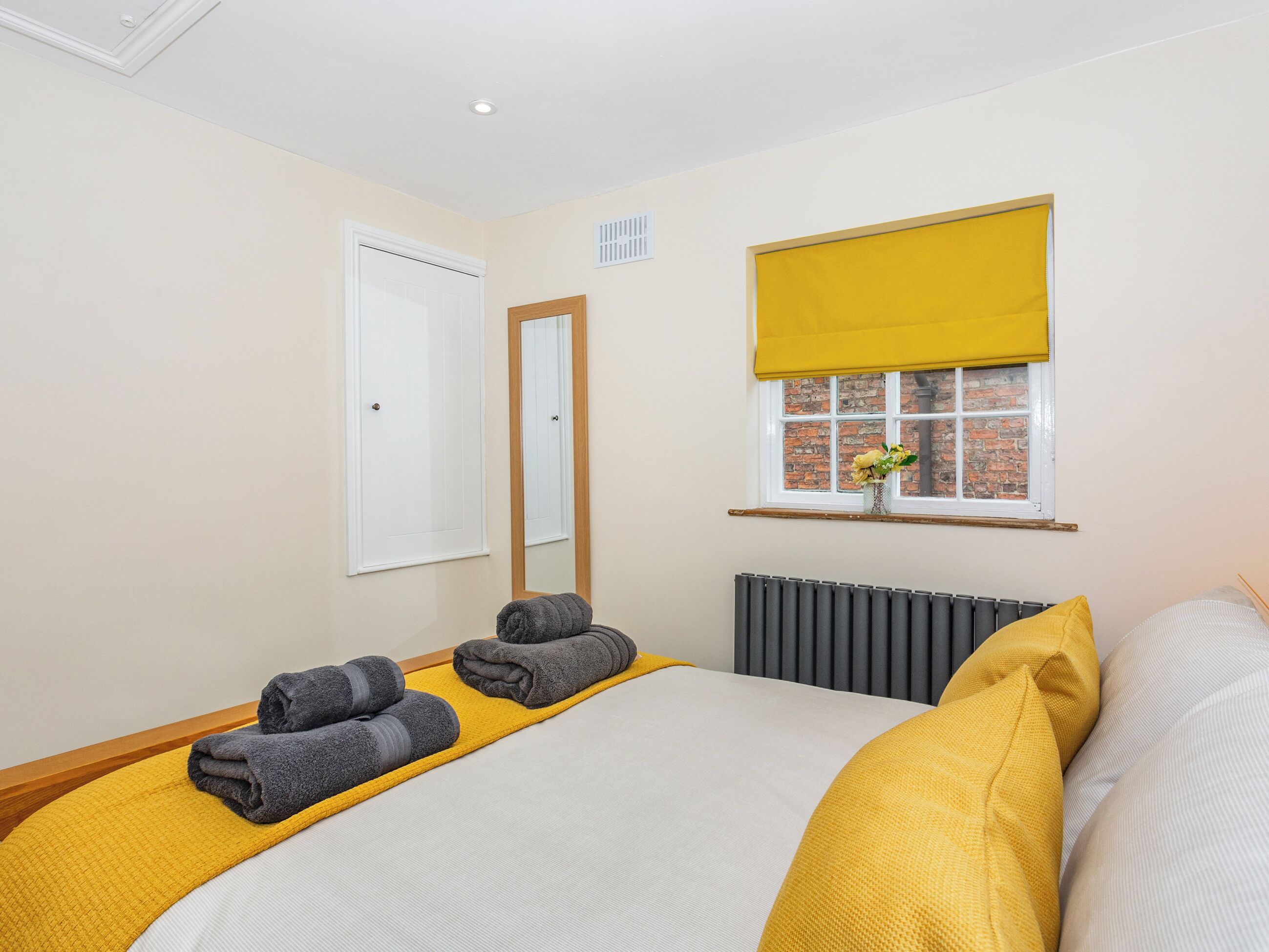 A hotel room with a bed, a window with a view of a brick building, a radiator, and a door.