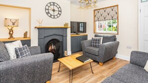 A modern living room with grey sofas, a fireplace, a wall clock, and a chandelier. - 2 bedroom accommodation in Ripon (Ripon)
