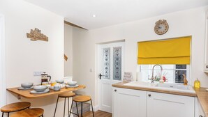A modern kitchen with white cabinets, a wooden countertop, and a yellow window blind. There are stools and a table with bowls and cups. - 2 bedroom accommodation in Ripon (Ripon)