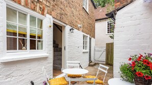 A small courtyard with a white brick building, a white door, a set of stairs, and a table with yellow cushions. - 2 bedroom accommodation in Ripon (Ripon)