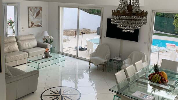 A modern living room with a glass coffee table, white sofas, a dining table with fruit, and a large window overlooking a pool. - Cannes Villa center pool spa classified (Cannes)