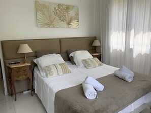 Un lit bien fait, avec des draps blancs et deux oreillers, une lampe de chevet, une télécommande et une serviette enroulée posée sur le lit.
