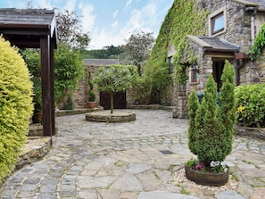 Un patio con pavimento de piedra, una pérgola de madera y diferentes plantas en macetas.