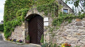 Een stenen gebouw met een donkerhouten deur en borden die aangeven dat het een tuinhuis is.