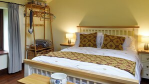 Een slaapkamer met een houten bed, witte beddengoed, een nachtkastje met een lamp, een houten ladder en een mand.