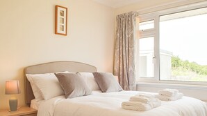 A neatly made bed with pillows, a bedside lamp, and a window with curtains. - 3 bedroom accommodation in Fishguard (Fishguard)