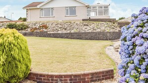 A two-story house with a stone retaining wall and a grassy lawn. - 3 bedroom accommodation in Fishguard (Fishguard)