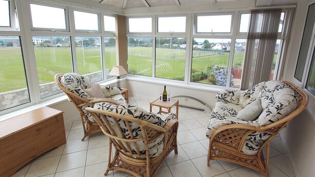 A conservatory with wicker furniture, a wooden bench, and a view of a green field. - 3 bedroom accommodation in Fishguard (Fishguard)