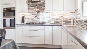 A modern kitchen with white cabinets, a stainless steel range hood, a double oven, and a tiled backsplash. - 3 bedroom accommodation in Fishguard (Fishguard)