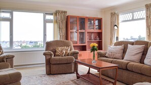 A living room with a sofa, armchair, and a wooden coffee table. There is a cabinet with glass doors and a vase with yellow flowers. - 3 bedroom accommodation in Fishguard (Fishguard)