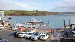 Un porto turistico con imbarcazioni ormeggiate, un'area parcheggio con auto e vista sull'acqua e le colline sullo sfondo.