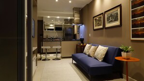A modern living room with a blue sofa, a small round table with a plant, and a kitchen in the background. - #3 Sophisticated Studio on Boaventura Da Silva (PA)