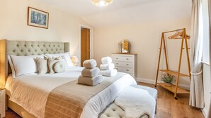 A bedroom with a large bed, a bedside table, a dresser, a hanging clothes rack, and a ceiling light.