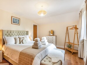 A bedroom with a large bed, a bedside table, a dresser, a hanging clothes rack, and a ceiling light.