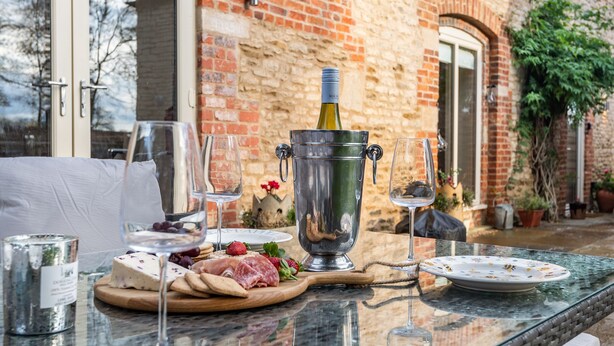 A glass table with a bottle of wine, glasses, and a cheese board with various cheeses and crackers.