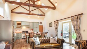 A spacious living room with a leather sofa, wooden flooring, and a kitchen in the background.