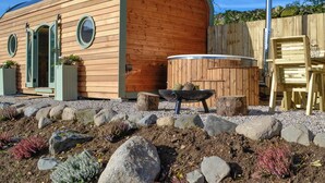 A wooden cabin with a curved roof, a hot tub, and a deck with chairs. - A hidden gem in the stunning Ayrshire countryside. (Straiton, near Maybole)