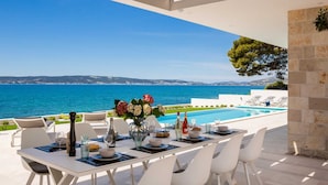 Comedor con mesa lista para cuatro personas, con vista a una piscina y al mar.