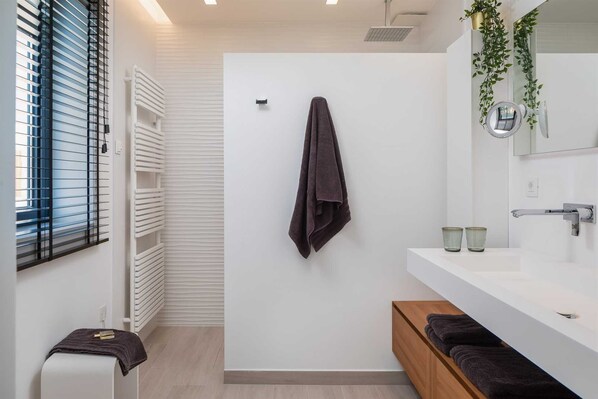 Un baño moderno con un tocador blanco, una toalla colgada en la pared y una ventana con persianas.