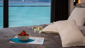 Un dormitorio con vista al mar, un cuenco de fresas, dos copas de vino blanco y una almohada.