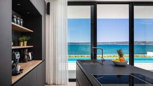 Una cocina moderna con vistas al mar, que cuenta con un ventanal grande, una estufa integrada y un bol de fruta en la encimera.